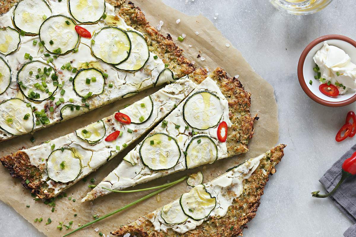 Low Carb Pizza mit Zucchini belegt auf hellem Untergrund