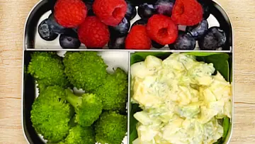 Gekochte Brokkoliröschen, bunte Beerenmischung aus Himbeeren und Heidelbeeren sowie cremiger Eiersalat auf Spinatblättern, sortiert in einer Edelstahl-Lunchbox. - Foto: LECKER @ Bauer Media Group