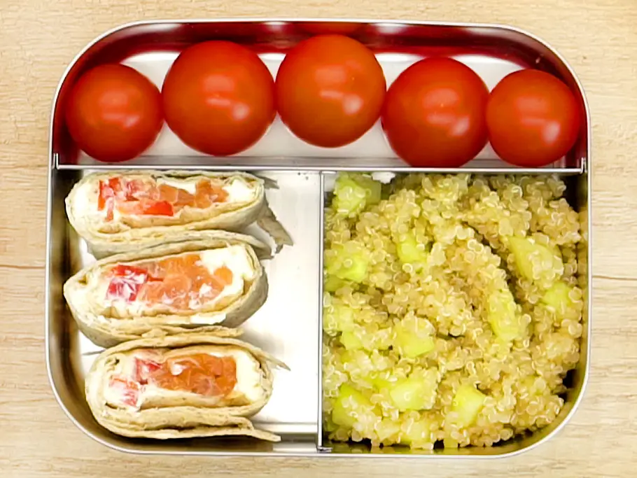 Drei Wrapstücke mit Frischkäse und Gemüse, dazu Kirschtomaten und Quinoa-Salat mit Gurke appetitlich in einer Edelstahl-Lunchbox angerichtet.