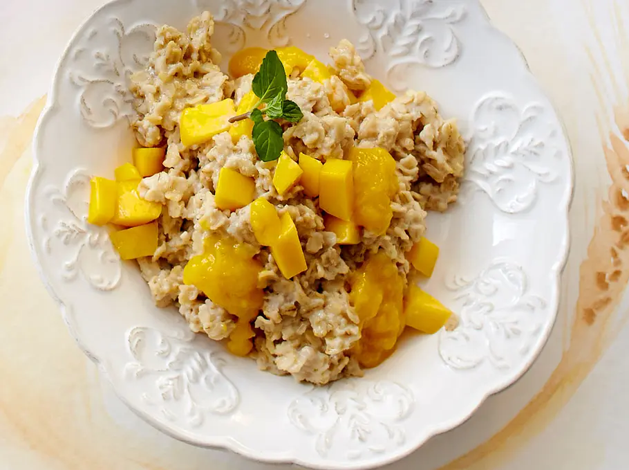 Mandel-Hafer Brei Mandel-Hafer-Brei mit Mango und Minze auf einem weißen Teller mit Ornamenten.