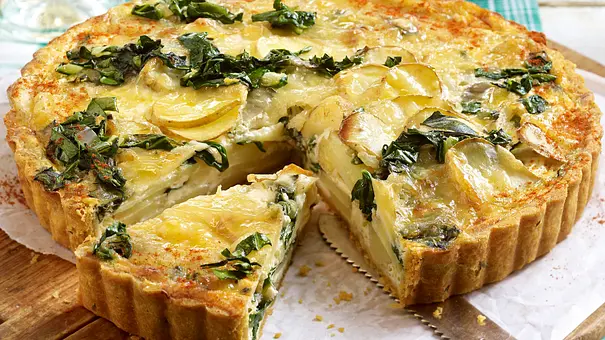 Angeschnittene Mangold-Kartoffel-Quiche wird auf einem runden Holzbrett serviert. - Foto: LECKER @ Bauer Media Group