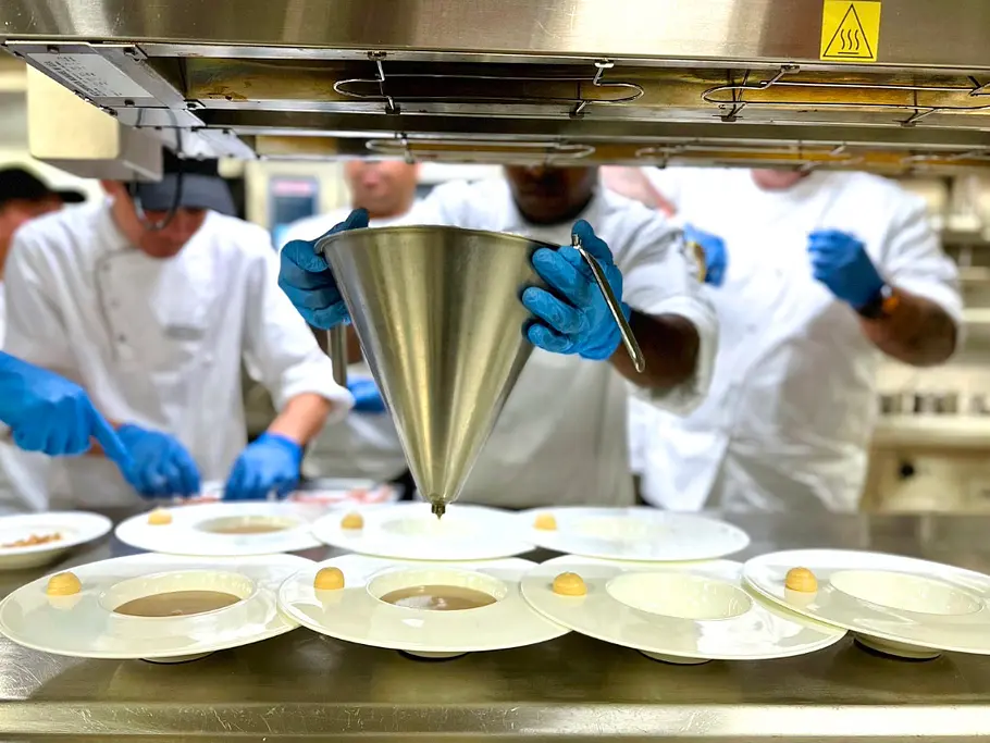 Maronensuppe wird in der AIDAnova-Bordküche von mehreren Köchen durch einen großen Trichter in die Suppenschüsseln gefüllt 