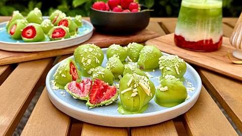 Erdbeeren umhüllt von Matcha-Schokolade auf Tellern mit frischen Erdbeeren und einem Iced Strawberry Latte im Hintergrund - Foto: Franziska Hoppe / LECKER.de