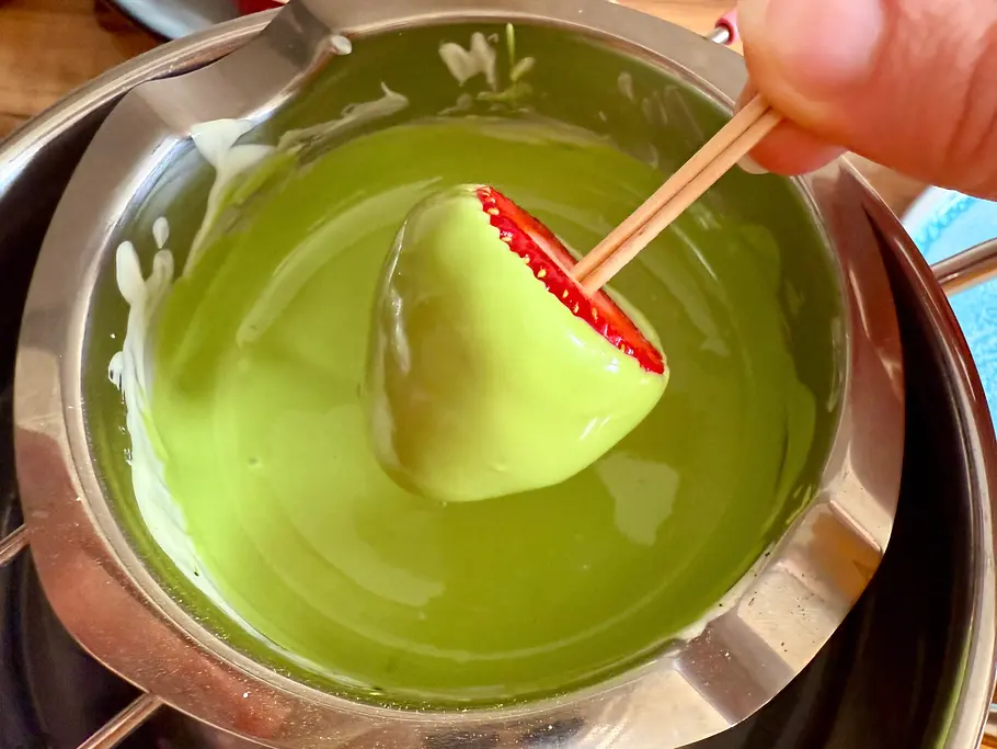 An den Zahnstochern halte ich die Erdbeeren fest und tauche sie in die Matcha-Schokolade.