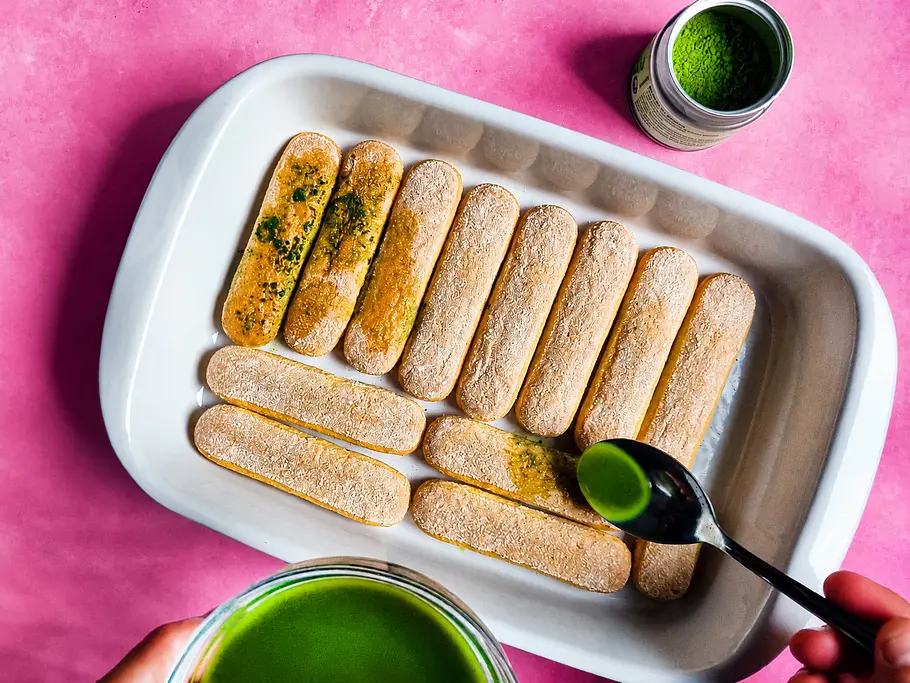 Matcha-Tiramisu zubereiten Matcha-Tee wird mit einem Esslöffel über die Biskuits geträufelt.