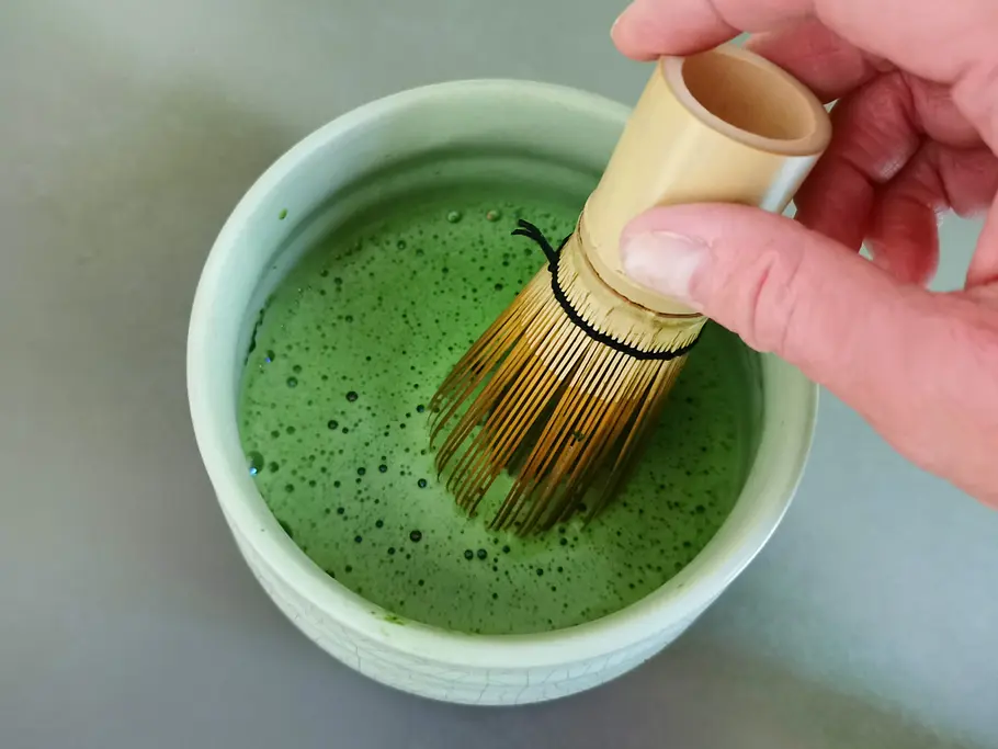 Matcha mit Wasser mit einem Matchabesen verrühren