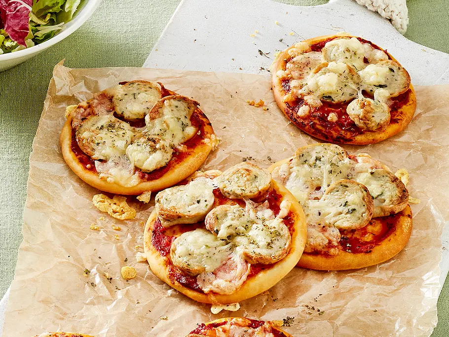 Mini Weißwurst-Pizzen Rezept Kleine Pizzen mit Weißwurst und Käse liegen auf Backpapier.