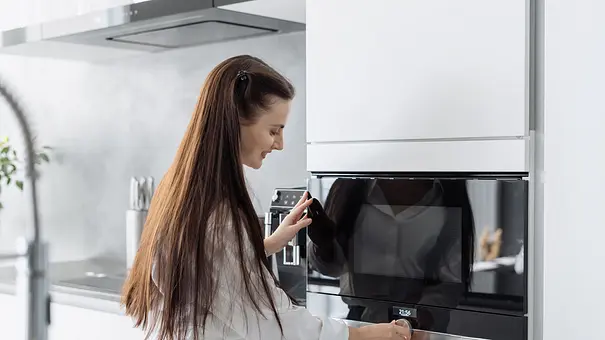 Eine junge Frau programmiert die Mikrowelle. - Foto: iStock / brizmaker Eine junge Frau programmiert die Mikrowelle. - Foto: iStock / brizmaker