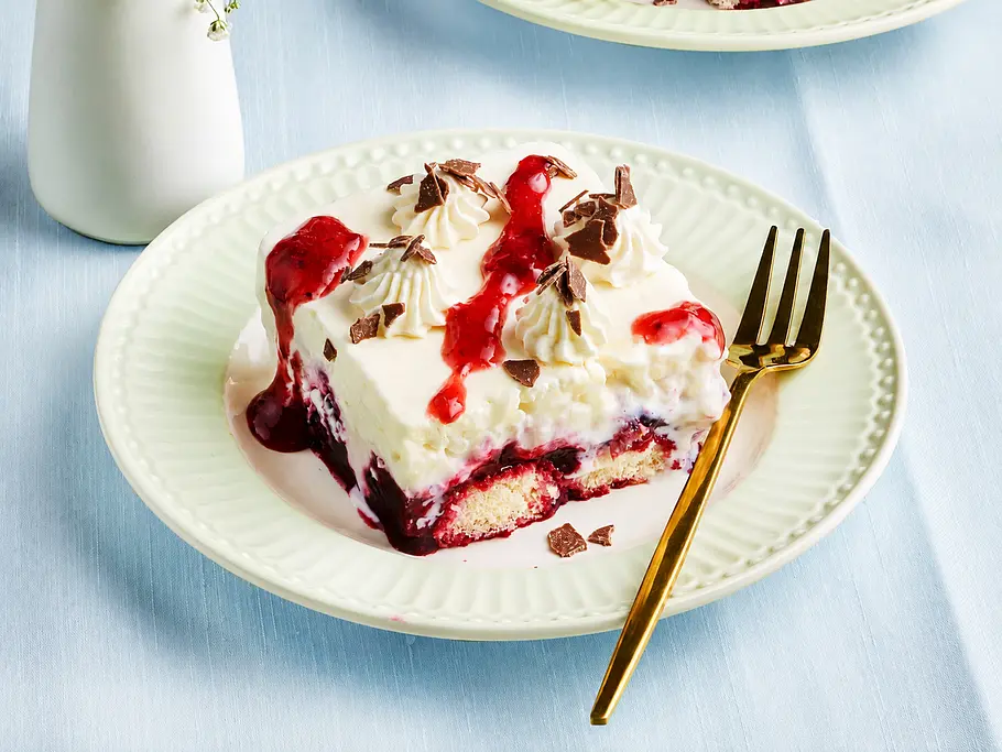Milchreis-Tiramisu mit Beeren Ein Stück Milchreis-Tiramsiu mit Beerensoße und Schokoraspel auf einem Teller.