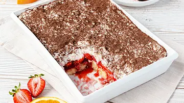 Das Milchreis-Tiramisu ist in einer Auflaufform geschichtet. Ein Stück ist entnommen. Man sieht Erdbeeren, Erdbeersoße, Milchreis und die Löffelbiskuits. - Foto: ShowHeroes für LECKER @ Bauer Media Group
