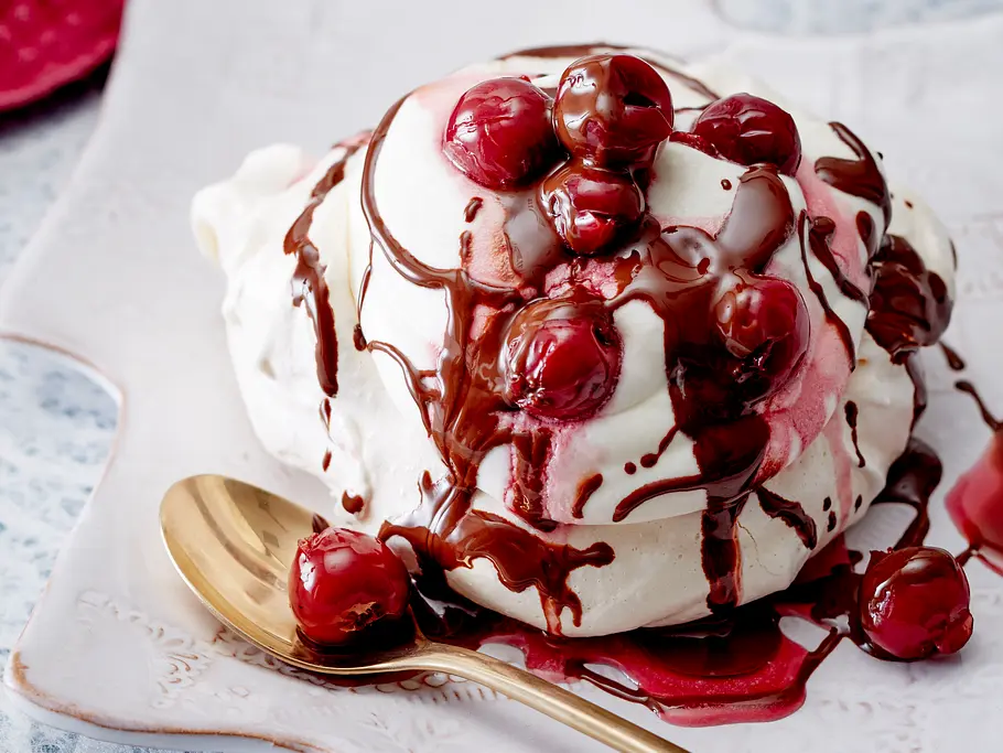 Mini-Pavlova auf einem Servierteller, Kirschen und Schokoladensoße als Topping