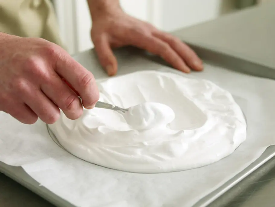 Mit einem Löffel wird in den Eischnee-Kreis auf Backpapier eine Mulde in der Mitte geformt.