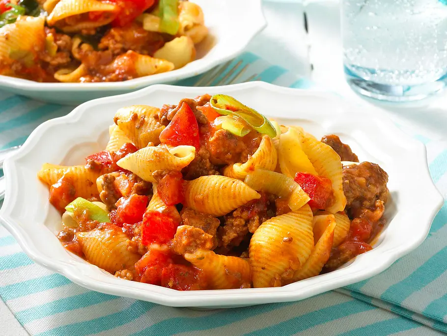 Muschelnudeln mit Hacksoße Rezept Eine weiße Schüssel mit Muschelnudeln, Hackfleischsoße und Paprikawürfeln.