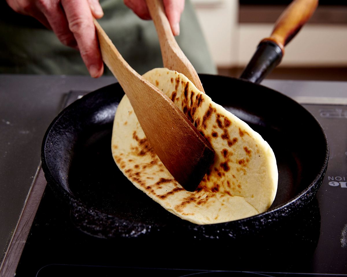 Naan-Brot mit einem Pfannenwender wenden