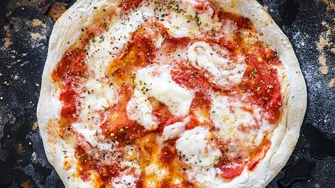 Neapolitanische Pizza mit Tomatensauce und Mozzarella auf bemehlter schwarzer Schieferplatte. - Foto: House of Food / Bauer Food Experts KG