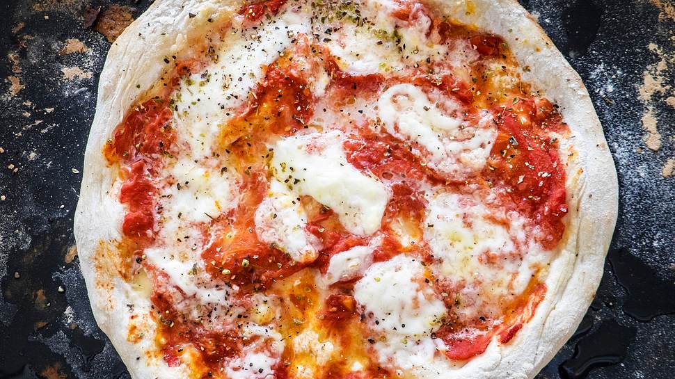 Neapolitanische Pizza mit Tomatensauce und Mozzarella auf bemehlter schwarzer Schieferplatte. - Foto: House of Food / Bauer Food Experts KG