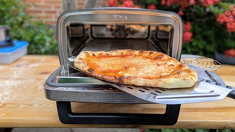 Eine goldbraun gebackene Pizza Margherita wird mit einem Schieber aus dem Ninja Artisan Outdoor-Elektro-Pizzaofen geholt. - Foto: Emily Beckmann / LECKER.de