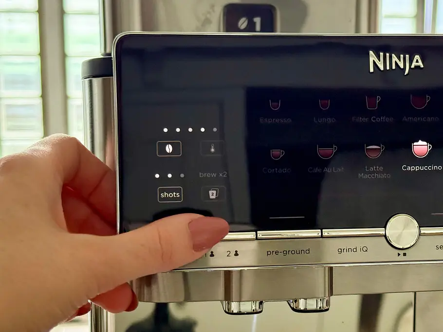 Ninja AutoBarista Pro Benutzerprofile Das Disolay der Ninja AutoBarista Pro und eine Hand, die auf den Knopf für die Benutzerprofile drückt.