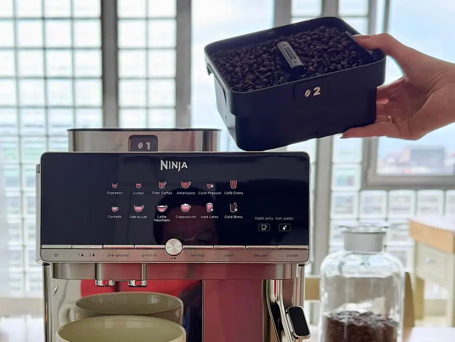 Ninja AutoBarista Pro Bohnenbehälter Ein Bohnenbehälter ist auf der Ninja AutoBarista Pro montiert, der zweite wird von einer Hand danebengehalten.