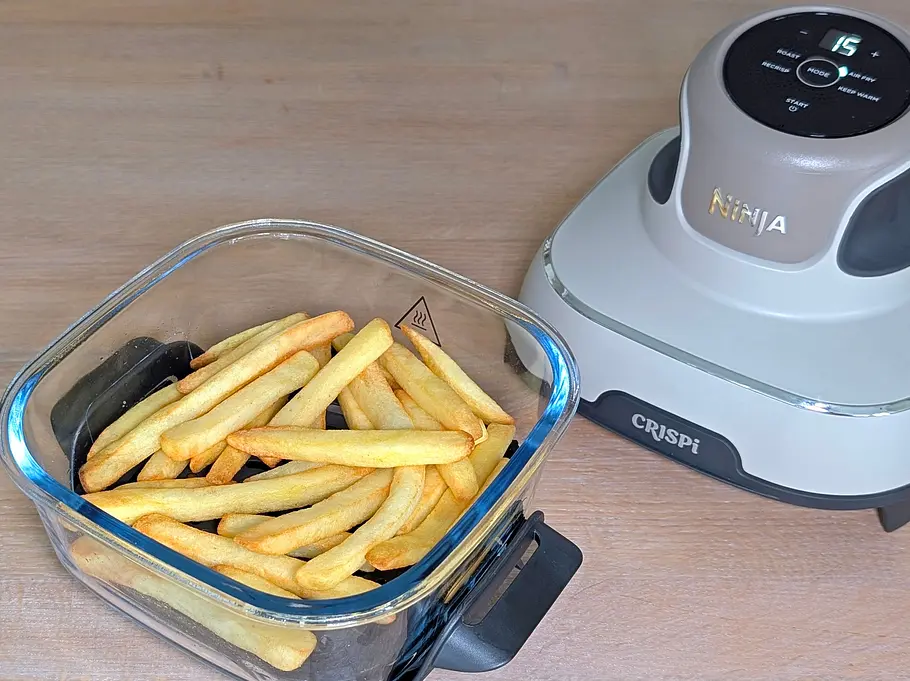 Rechts auf einer Arbeitsfläche steht der Pod-Aufsatz der Ninja Crispi Heißluftfritteuse. Links daneben die kleine Glasschale mit ungleichmäßig gebackenen TK-Pommes.