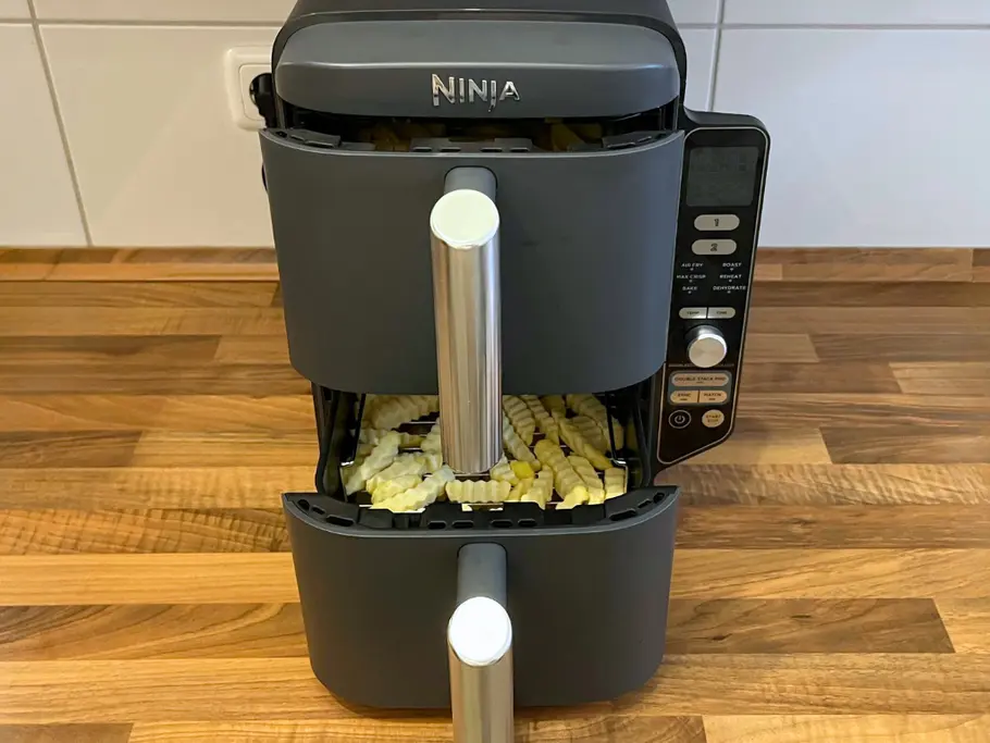 Ninja Double Stack XL im großen Test Der Ninja Double Stack XL Airfryer steht mit leicht geöffneten Schubladen auf einer hölzernen Küchenanrichte, sodass man sieh, dass beide Schubladen mit TK-Pommes gefüllt sind