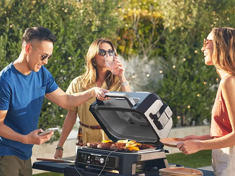 So schmeckt der Sommer – mit den Neuheiten von Ninja Zwei Frauen und ein Mann stehen um einen Grill herum im Garten
