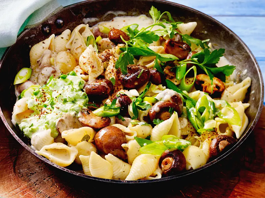 Nudeln mit cremiger Champignonsoße in einer Pfanne, garniert mit Lauchzwiebeln und Erbsen-Dip.
