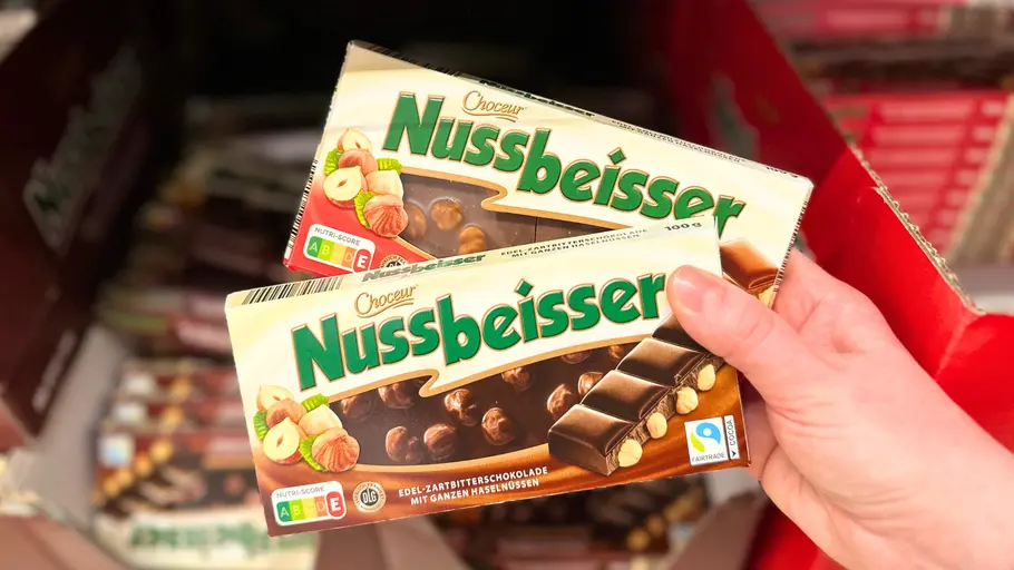 Eine Hand hält eine helle Vollmilch-Variante und eine dunkle Zartbitter-Variante der Aldi-Nussbeißer-Schokolade von Choceur