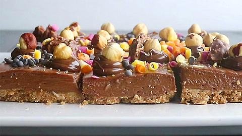 Nutella-Cheesecake vom Blech in quadratische Stücke geschnitten und mit Haselnüssen getoppt. - Foto: ShowHeroes