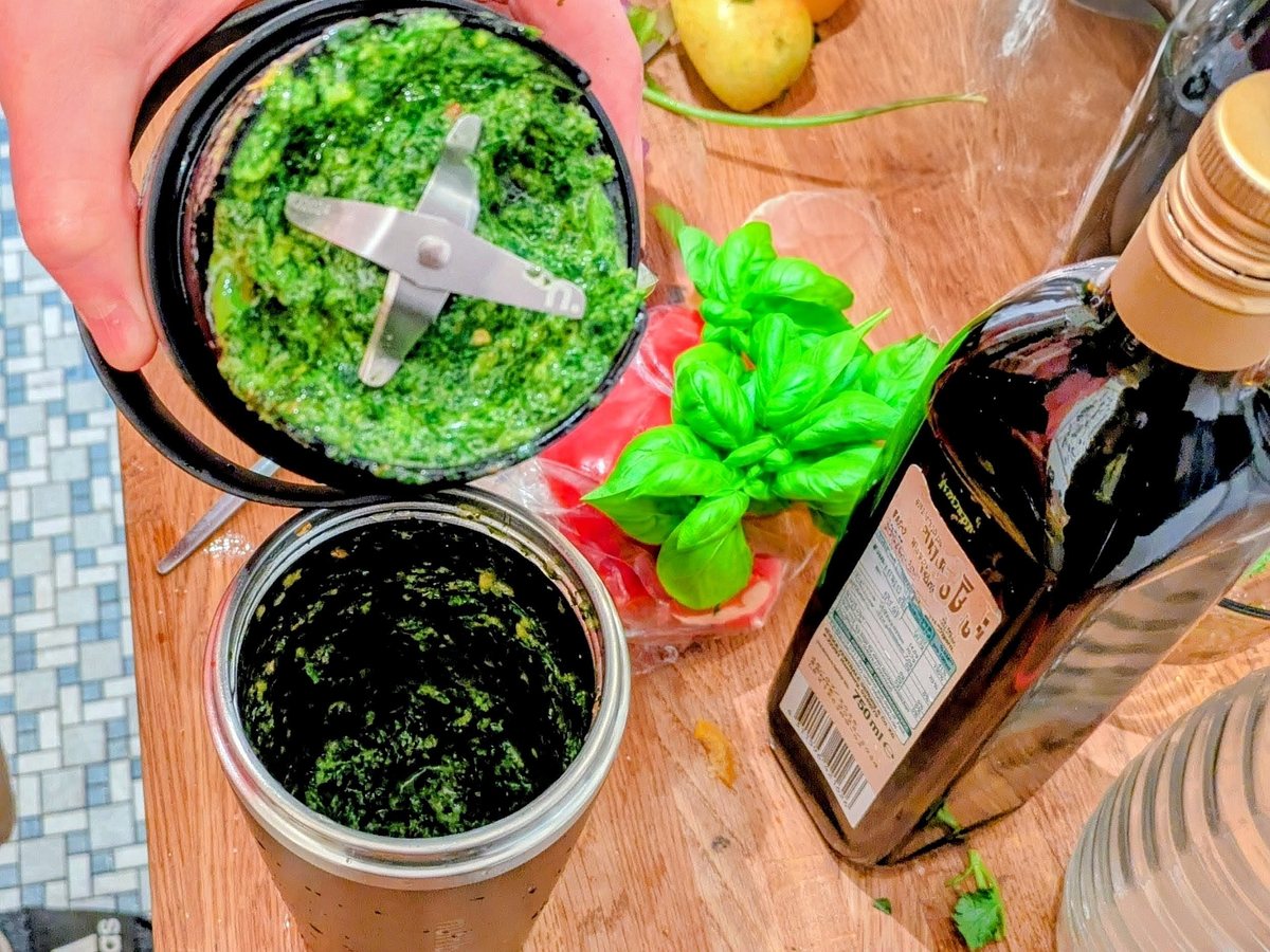 nutribullet Flip Smoothie-Maker Pesto Der Mixaufsatz wird vom nutribullet Flip Smoothie-Maker abgenommen, im Behälter befindet sich frisches grünes Pesto, daneben steht Olivenöl.