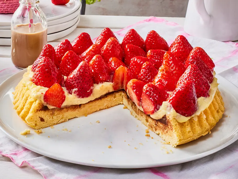 Erdbeerkuchen mit Vanillecreme Saftiger Obstboden aus Rührteig, dick mit cremiger Vanillecreme bestrichen und frisch belegten, glänzenden Erdbeeren, angerichtet auf einer weißen Platte.