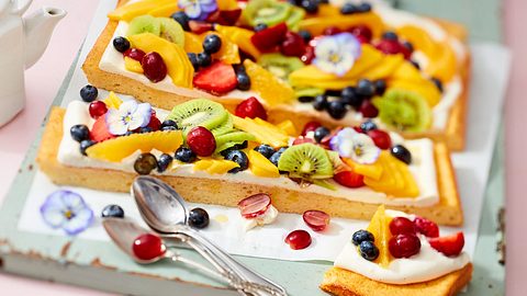 Längs-geschnittener bunter Obstsalat-Joghurt-Kuchen mit Blüten auf einem Servierbrett - Foto: House of Food / Bauer Food Experts KG
