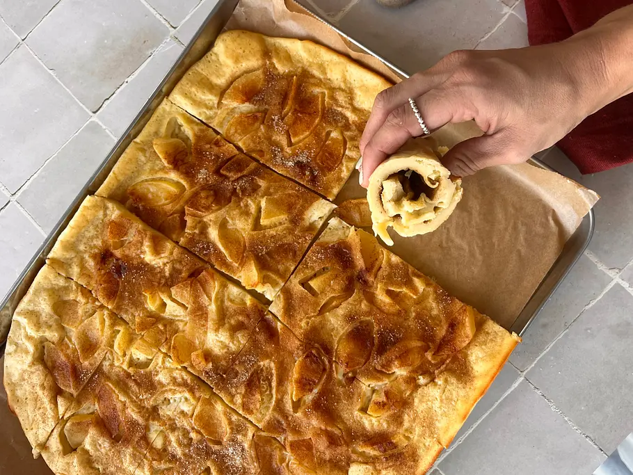Apfelpfannkuchen vom Blech mit einer Hand, die ein Stück eingerollt hält.