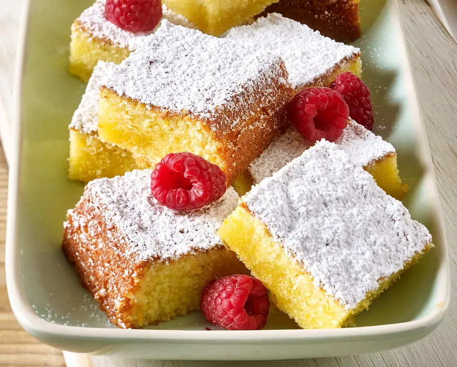Olivenölkuchen mit Orange Rezept Mehrere Stücke Olivenölkuchen mit Puderzucker bestäubt und frischen Himbeeren auf einer hellen Platte angerichtet.