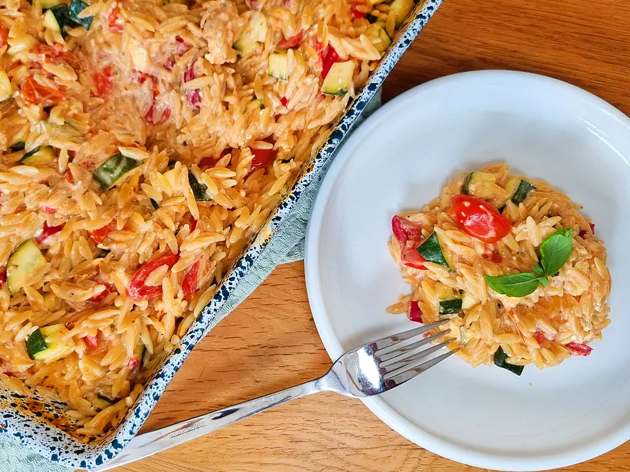 Fertige One-Pot Ofen-Kritharaki Cremige Ofen-Kritharaki auf dem Teller und in der Auflaufform.