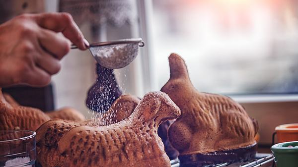 Ostergebäck in Lamm- und Hasenform wird mit Puderzucker bestreut - Foto: iStock/GMVozd