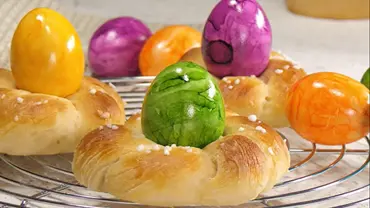Hefekränze mit bunten, glasierten Ostereiern in der Mitte, bestreut mit grobem Zucker, angerichtet auf einem runden Kuchengitter. - Foto: LECKER @ Bauer Media Group