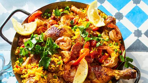 Spanische Paella mit gelbem Reis, Hähnchenkeulen, Garnelen, Erbsen, Paprika und Zitronenspalten, serviert in einer großen Pfanne mit Petersilie garniert. - Foto: House of Food / Bauer Food Experts KG