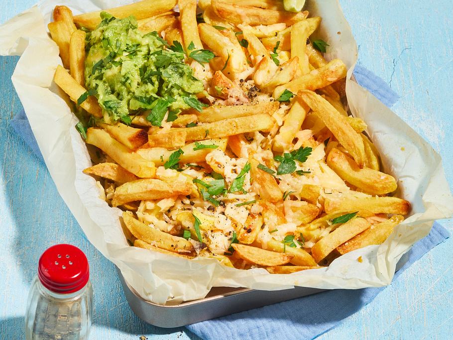 Parmesan-Knoblauch-Pommes liegen auf einem mit Backpapier ausgelegtem Blech und sind mit Guacamole angerichtet.