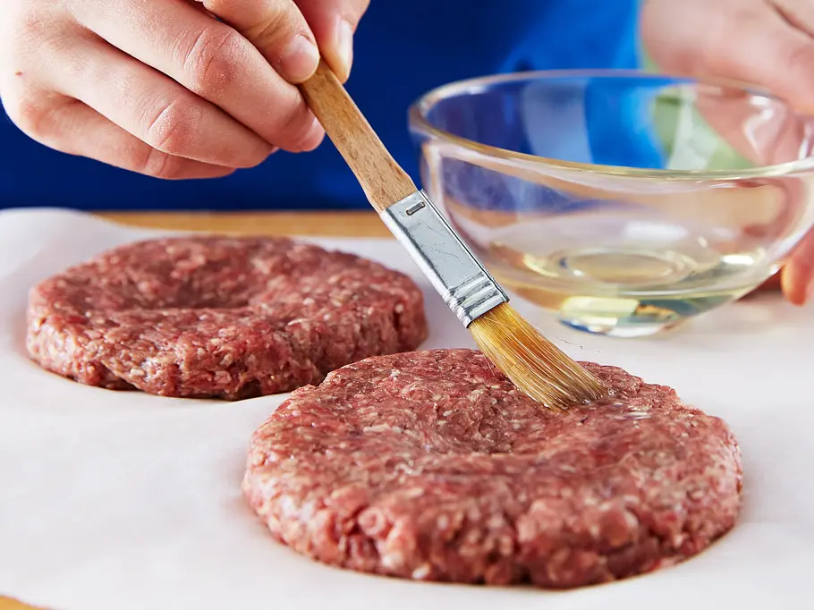 Burger-Patties werden mit Öl eingestrichen.