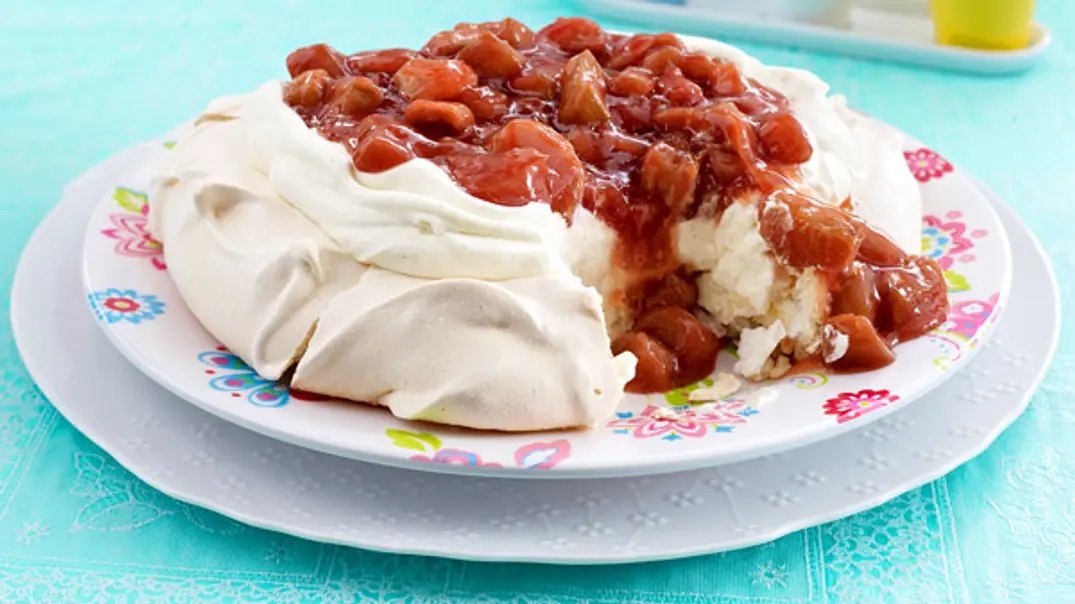 Eine Pavlova mit knusprigem Baiserboden, gefüllt mit Sahne und Rhabarberkompott, angerichtet auf einem bunten Teller, servierfertig auf einem hellblauen Tischtuch. - Foto: LECKER @ Bauer Media Group