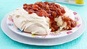 Eine Pavlova mit knusprigem Baiserboden, gefüllt mit Sahne und Rhabarberkompott, angerichtet auf einem bunten Teller, servierfertig auf einem hellblauen Tischtuch. - Foto: LECKER @ Bauer Media Group Eine Pavlova mit knusprigem Baiserboden, gefüllt mit Sahne und Rhabarberkompott, angerichtet auf einem bunten Teller, servierfertig auf einem hellblauen Tischtuch. - Foto: LECKER @ Bauer Media Group
