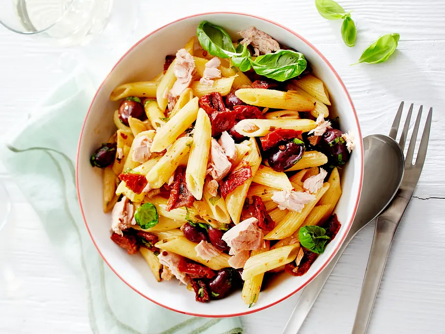 Penne Pomodoro e Tonno in einer weißen Schale daneben ein Esslöffel und eine Gabel