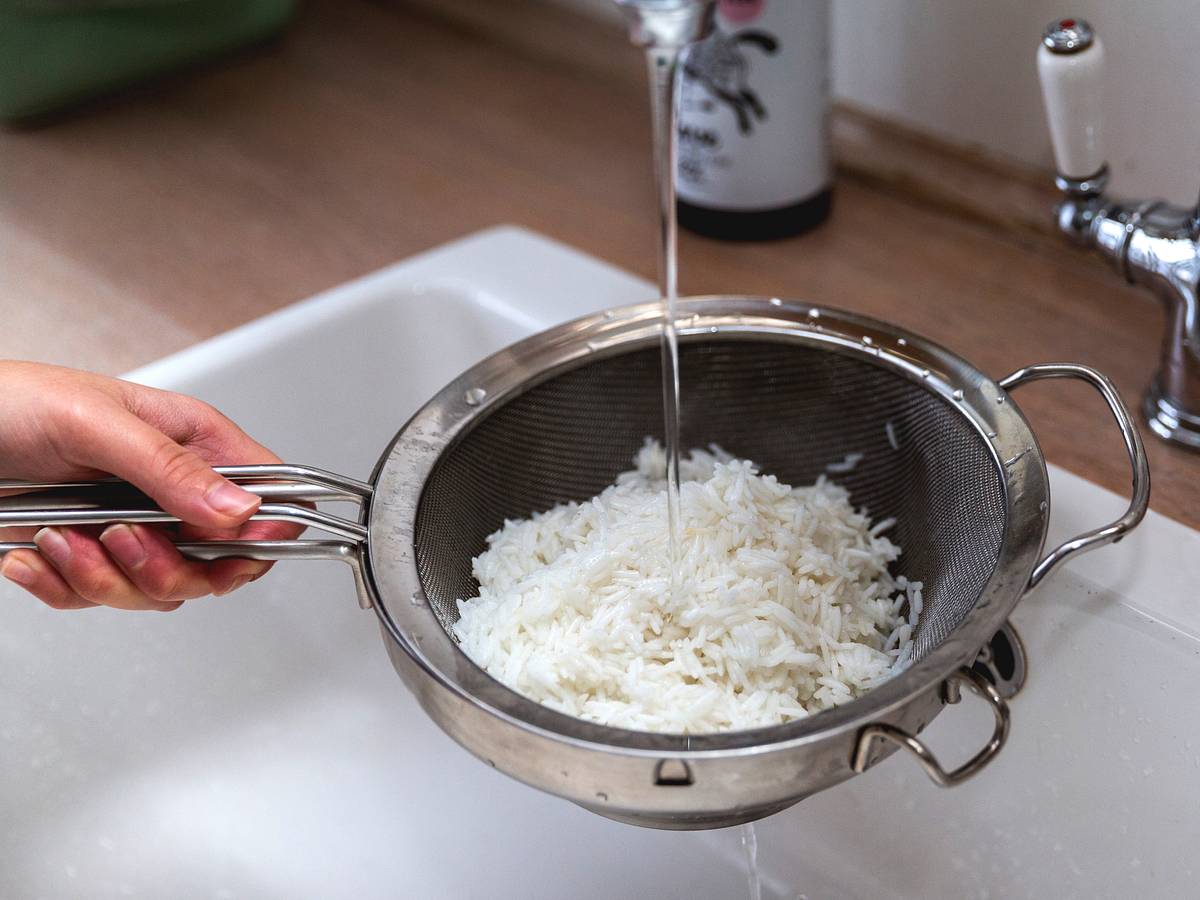 Vorgekochter Reis wird in einem Sieb unter kaltem Wasser abgeschreckt