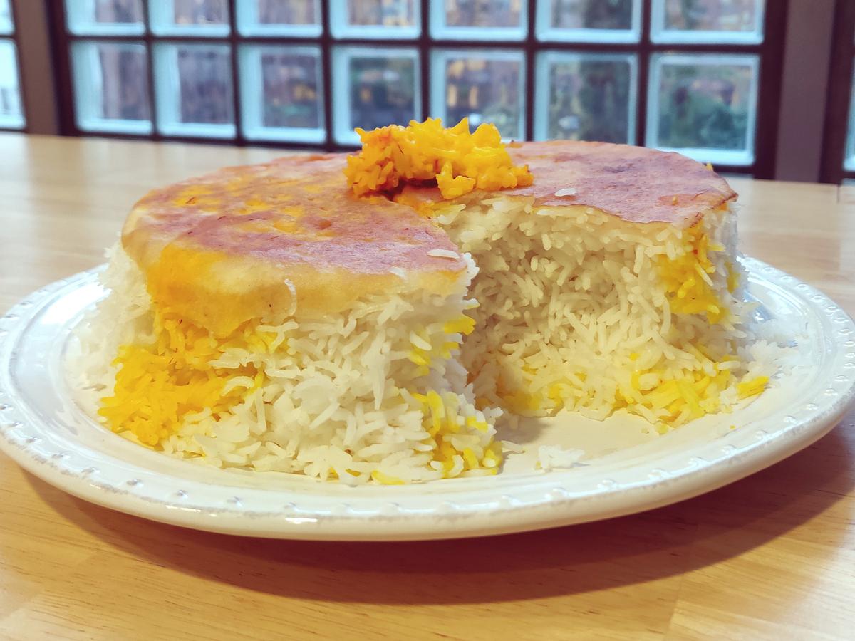 Persischer Reis mit Brot-Kruste liegt angeschnitten wie ein Kuchen auf einem Teller