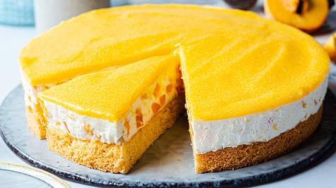 Die einfache Maracuja-Torte liegt auf einer Tortenplatte. Man erkennt den Anschnitt mit Aprikosenstückchen und den gelben Fruchtspiegel. - Foto: ShowHeroes