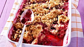 Pflaumen-Crumble in einer weißen, rechteckigen Auflaufform mit silbernem Löffel auf einem Küchentuch. - Foto: LECKER @ Bauer Media Group Pflaumen-Crumble in einer weißen, rechteckigen Auflaufform mit silbernem Löffel auf einem Küchentuch. - Foto: LECKER @ Bauer Media Group