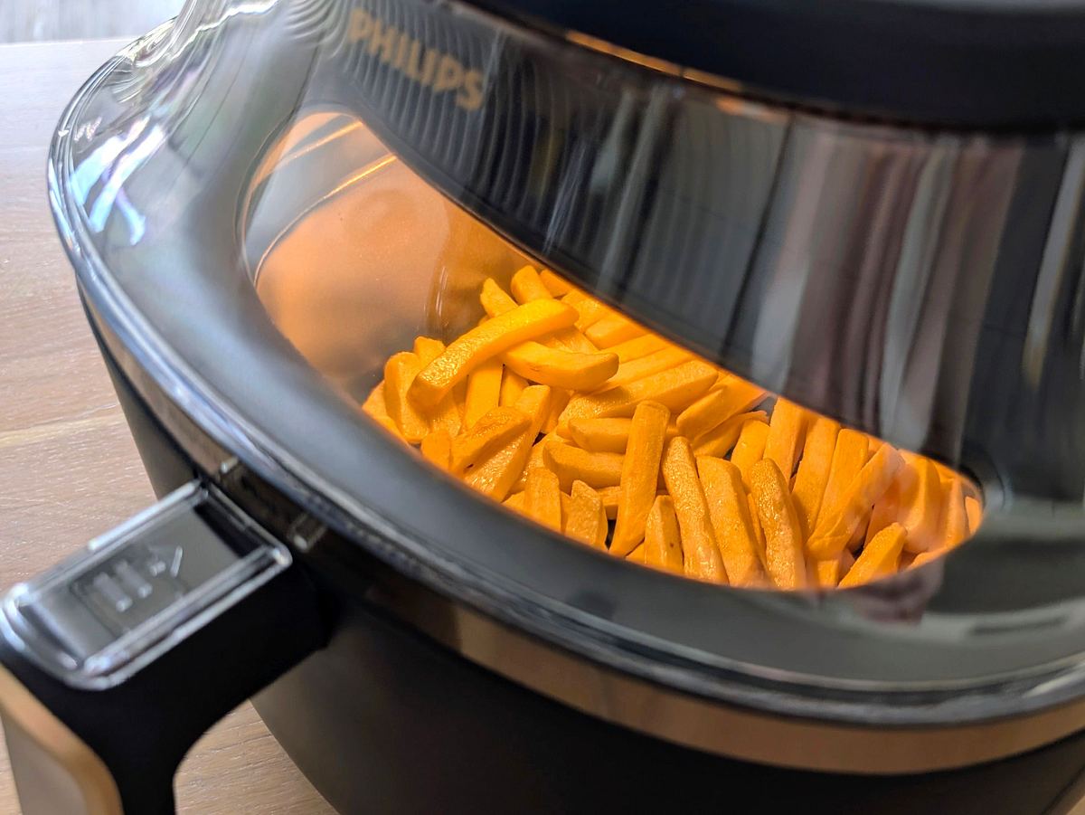 Blick von oben durch das Sichtfenster des Philips Airfryer 3000 Series NA332/00, in dem Licht brennt und Pommes garen.