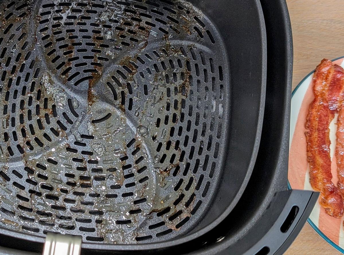 Blick von oben auf Fettrückstände im Innenkorb des Philips Airfryer 3000 Series 6,2 l. Am Rand liegen gebratene Bacon-Scheiben.