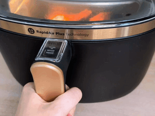 Eine Hand zieht die Schublade aus dem Philips Airfryer 3000 Series NA332/00 heraus. Darin liegen zwei gebackene, stark gebräunte Hähnchenschenkel.